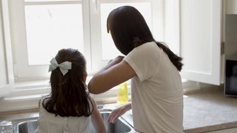 back view of mom and daughter washing dish together