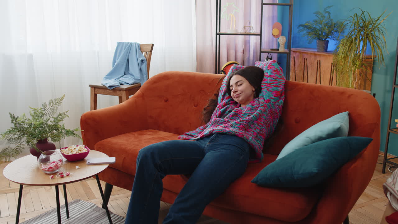Tired young woman lying down on comfortable couch taking a rest daytime nap relaxing falling asleep