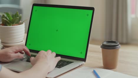 hands typing on laptop keyboard with green mock-up screen while sitting at the desk, video in 4k