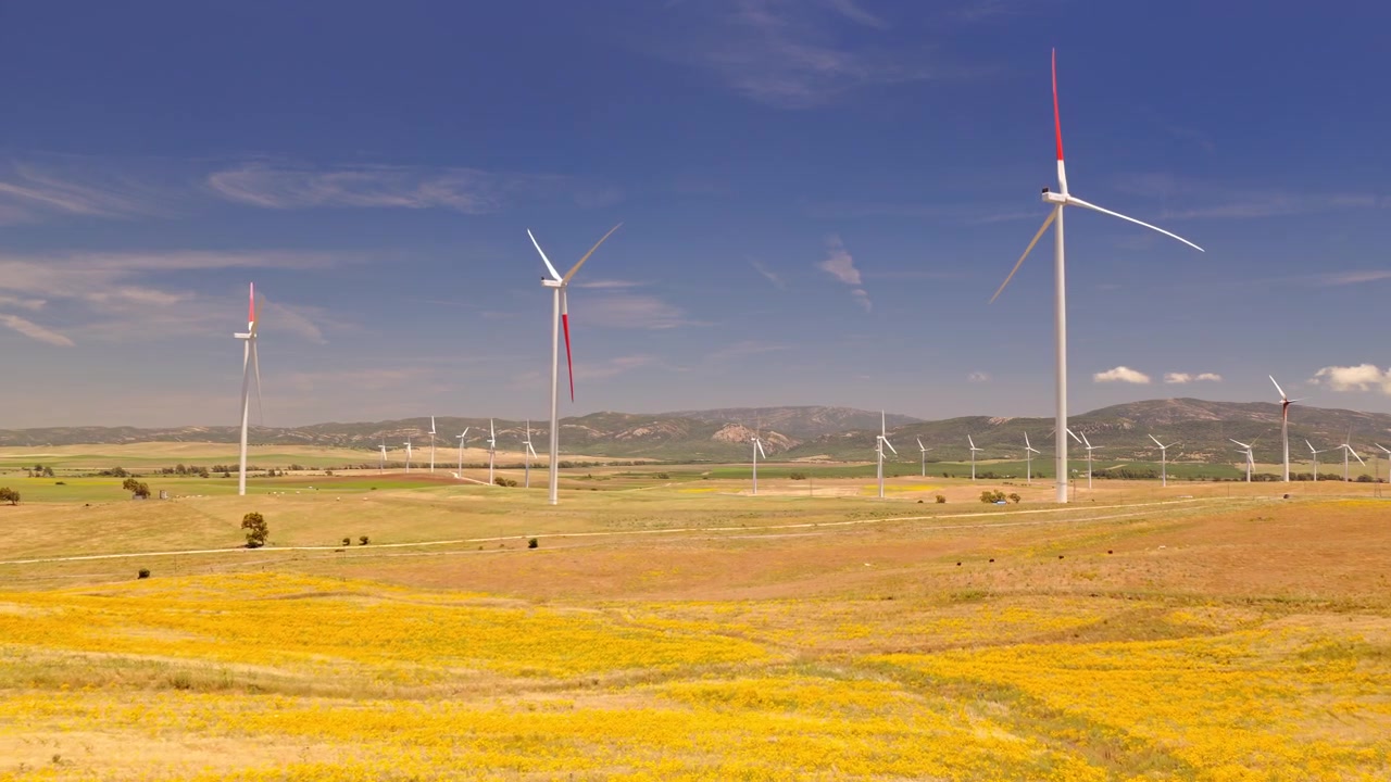 Filmato cinematografico con drone di un grande parco eolico con turbine che generano elettricità pulita e rinnovabile attraverso un paesaggio rurale. Infrastruttura energetica sostenibile a supporto della decarbonizzazione e degli obiettivi climatici