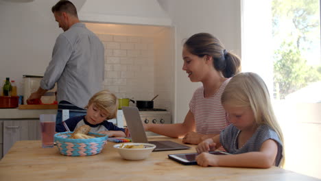 los niños en la mesa de la cocina con la mamá mientras el papá cocina