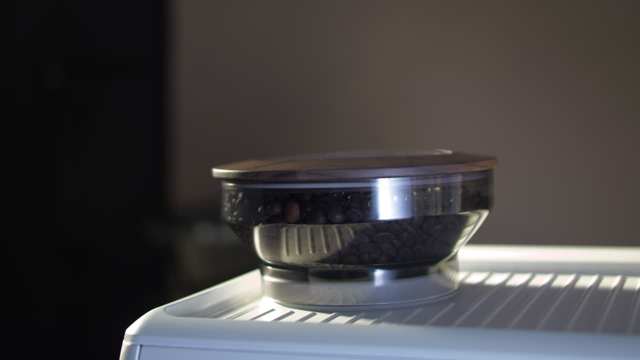 Close up of a hand placing a wooden lid onto a coffee grinder hopper filled with roasted beans. Warm light emphasizes natural wood texture, freshness, and the tactile espresso preparation ritual