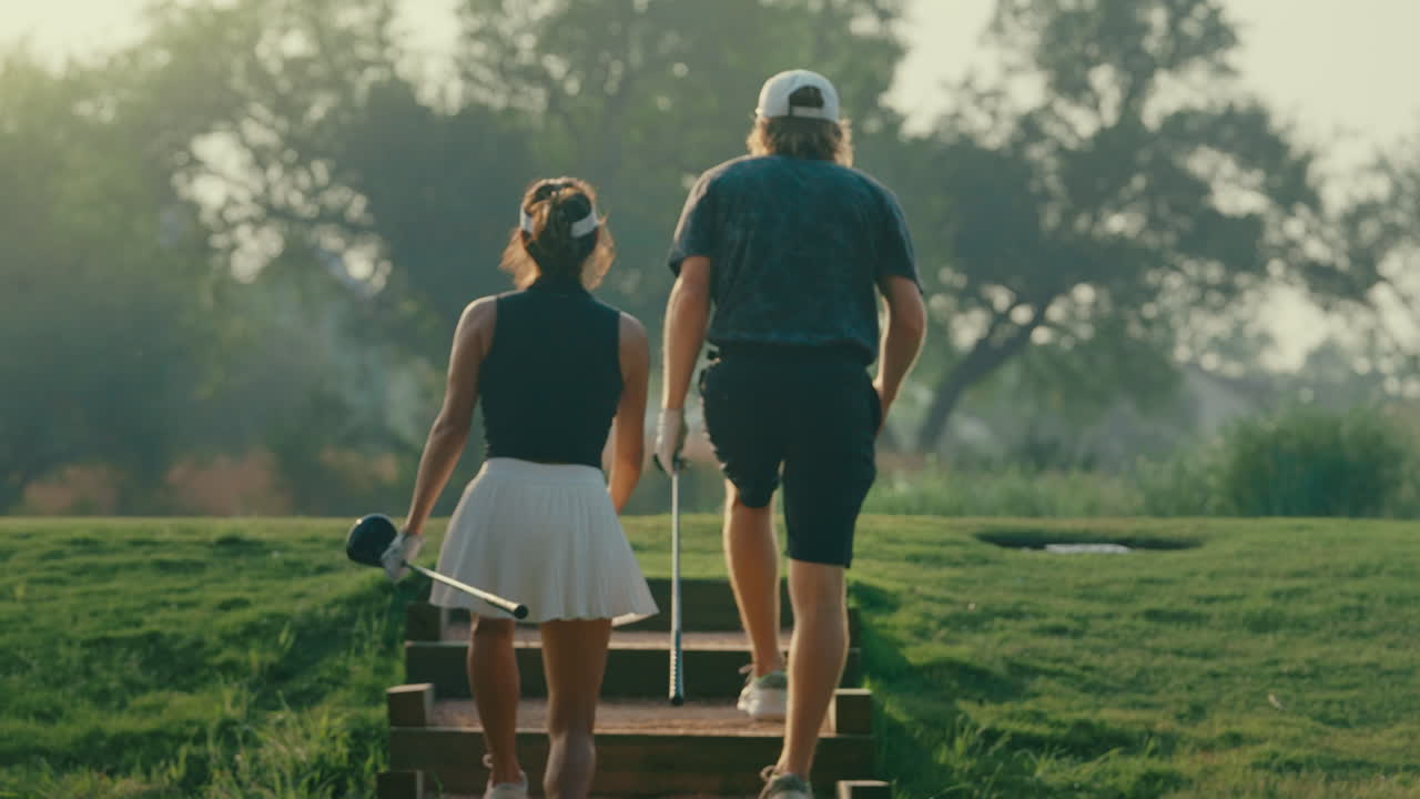 Couple walks slowly upstairs to the tee box in golden hour light after their playing partner hits a drive in the background. A cinematic moment capturing course atmosphere and relaxed game flow.