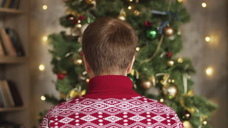 back view of man putting santa hat and decorating christmas tree at home