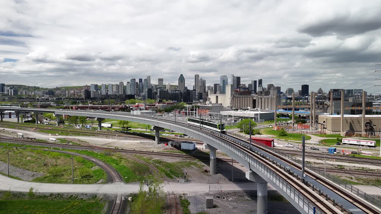 Aerial shot of downtown Montreal skyline under overcast sky, features REM train moving towards downtown area urban setting.