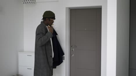 black man in front home door putting on trendy coat, leaving house, slow motion