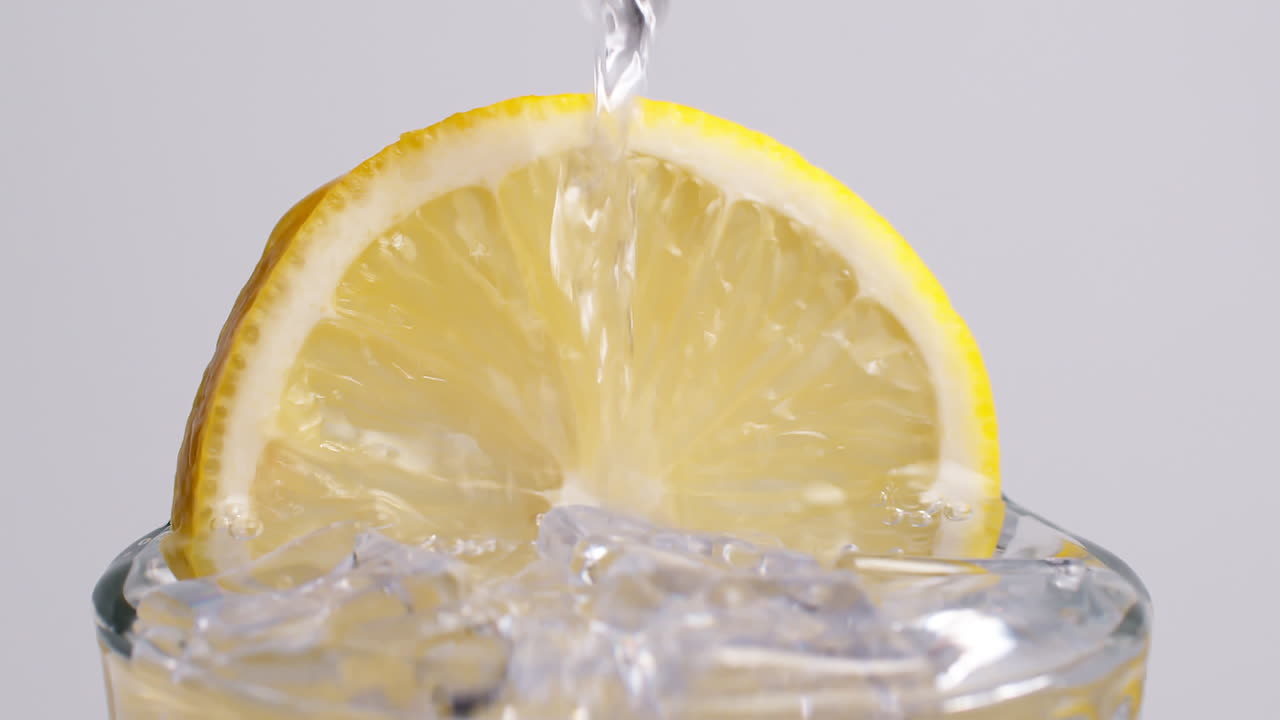 Acqua frizzante fredda e fresca che si versa in un bicchiere con ghiaccio e fette di limone