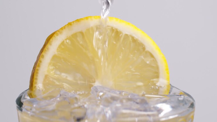 Acqua frizzante fredda e fresca che si versa in un bicchiere con ghiaccio e fette di limone