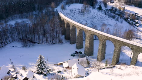 Rotating-view-of-a-stone-train-viaduct-above-a-village-in-winter-snow