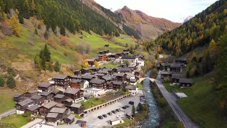 autumn view of larch forest in switzerland, with a church, town, mountains and a river on the background. sunny day. aerial footage