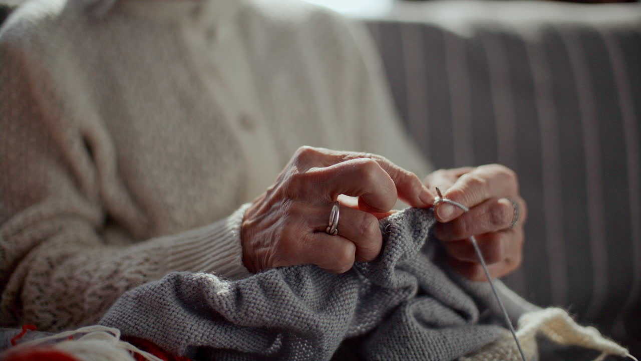 Elderly Woman Knitting with Yarn and Needles on Couch at Home