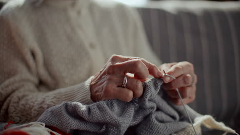 elderly woman knitting with yarn and needles on couch at home