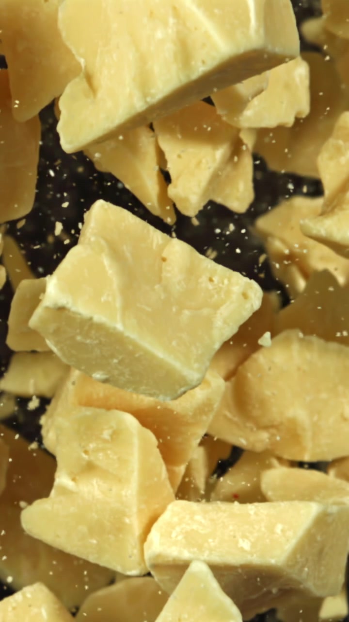 Morceaux de beurre de cacao tombant au ralenti sur fond noir.