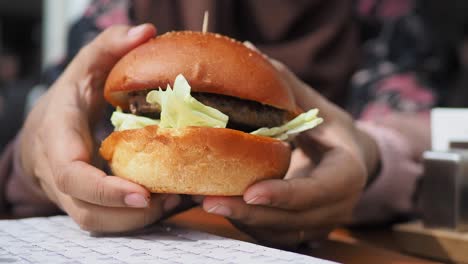 Mano-Sosteniendo-Hamburguesa-De-Ternera-En-La-Mesa-De-Cerca