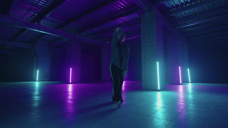 A-steel-woman-dances-hip-hop-freestyle-in-a-modern-style-in-a-hall-with-neon-light-in-purple-blue-colors.-Female-Professional-Hip-Hop-Dancer