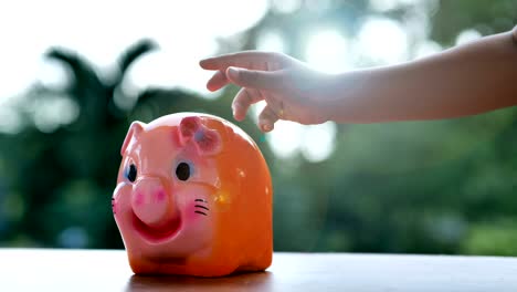 hand of child boy putting coins in a piggy bank, slow motion.  bokeh background. saving money and collecting money for the future.