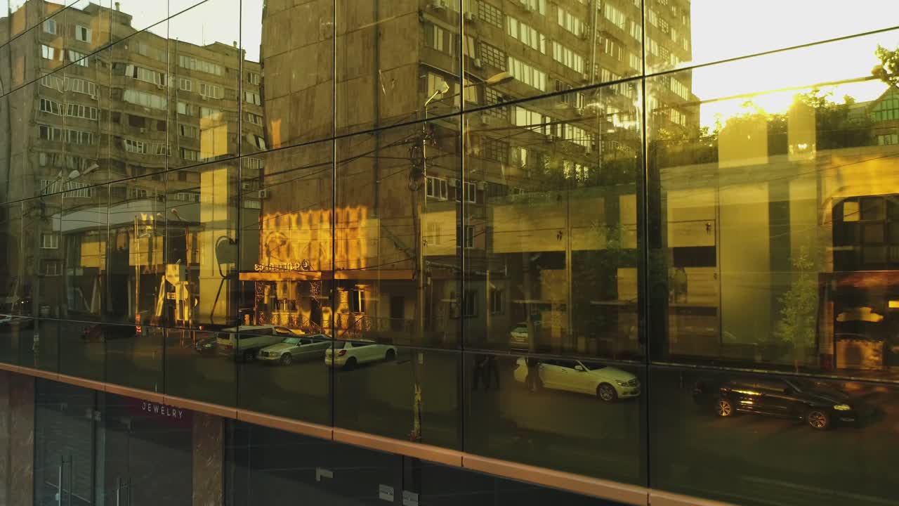 벽에 거울 창문이 있는 비즈니스 디스트릭트 빌딩이나 쇼핑몰의 4k 외관, 빛, 거울 벽에 있는 도시, 자동차 및 타워의 반사, 드론 카메라 이동