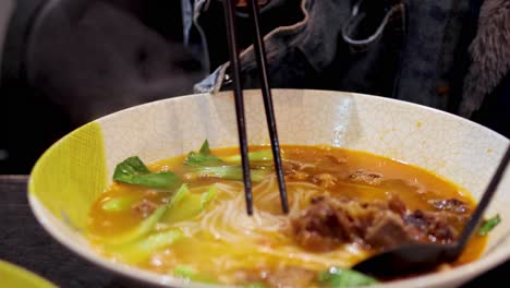 chopsticks lifting noodles from a spicy broth