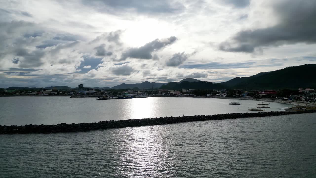 극적인 구름과 산악 배경을 가진 목가적인 방파제와 섬만의 실루엣의 공중 궤도 전망