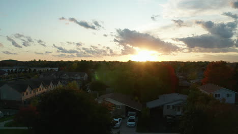 aerial view ascending over the suburbs at golden hour, with the sun in the distance setting and creating a beautiful lens flare