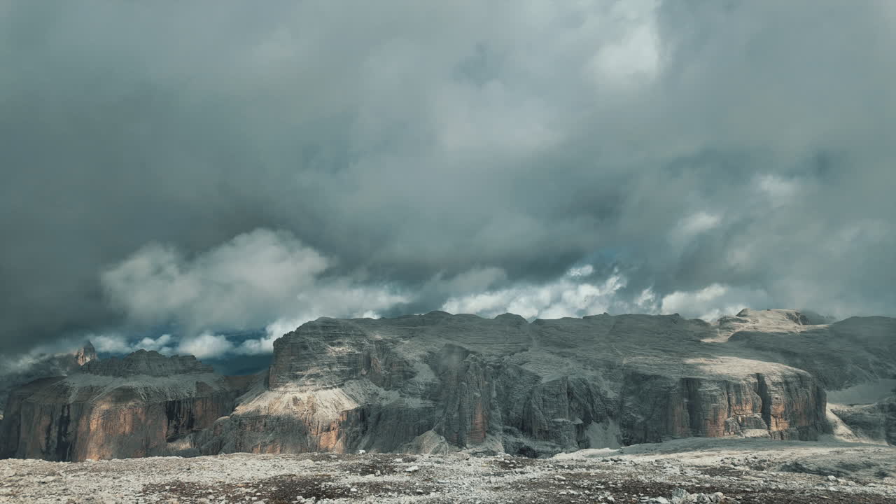 Dramatic cloudscape sweeping across rocky Dolomites terrain at Pordoi Pass, revealing dramatic mountain landscape transforming through atmospheric movement