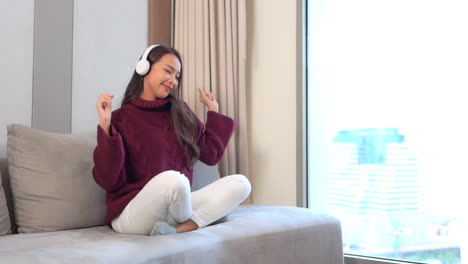 Woman-with-Headphones-Swinging-and-Dancing-on-Sofa-Listening-to-Music