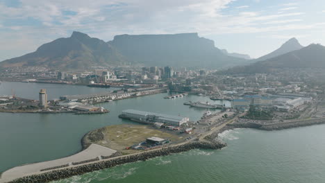 Fly-around-sea-coast.-Complex-of-building-in-Victoria-and-Alfred-Waterfront.-Flat-topped-mountain-ridge-above-city-in-background.-Cape-Town,-South-Africa