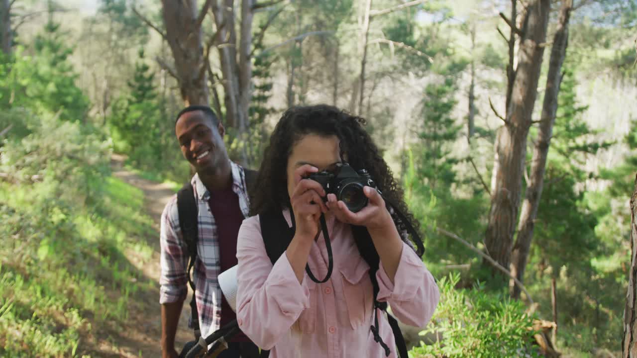 una pareja diversa sonriente tomando fotos y caminando por el campo