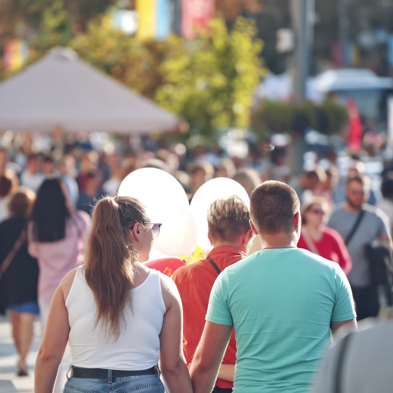 Pedestrian street filled with people. Citizens walking on the road in a bright summer day. Woman holding balloons while going downtown.