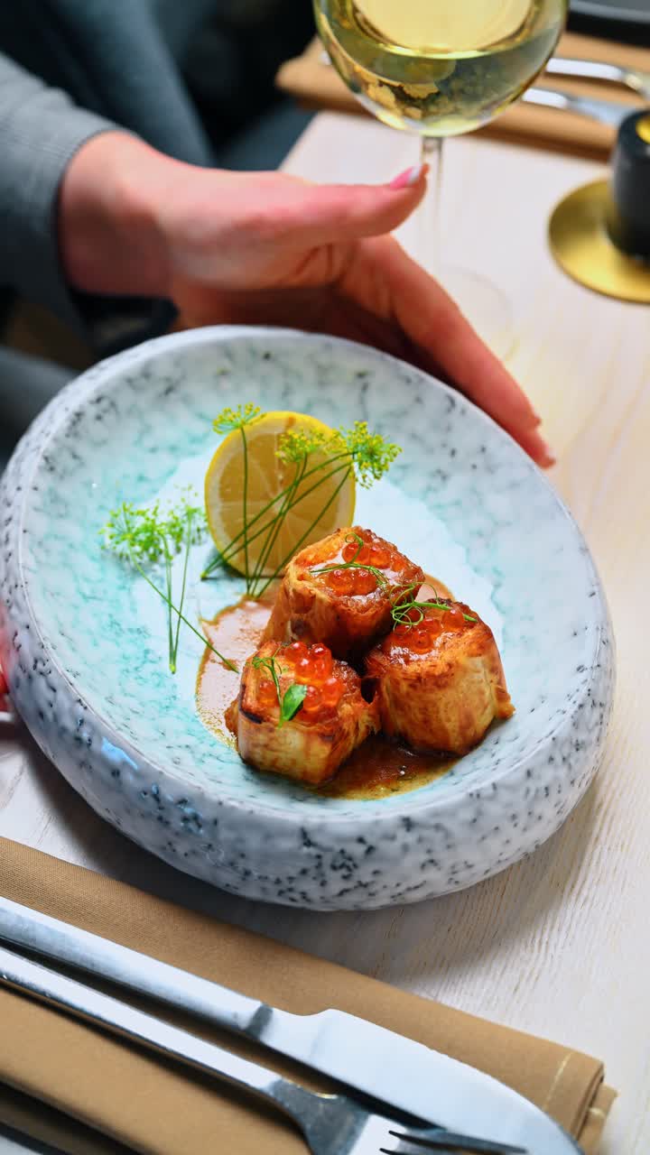 Hands of waitress serving plate of stuffed pancakes with caviar. Server presenting a blue textured plate with stuffed crepes topped with red roe and a lemon wedge in a restaurant