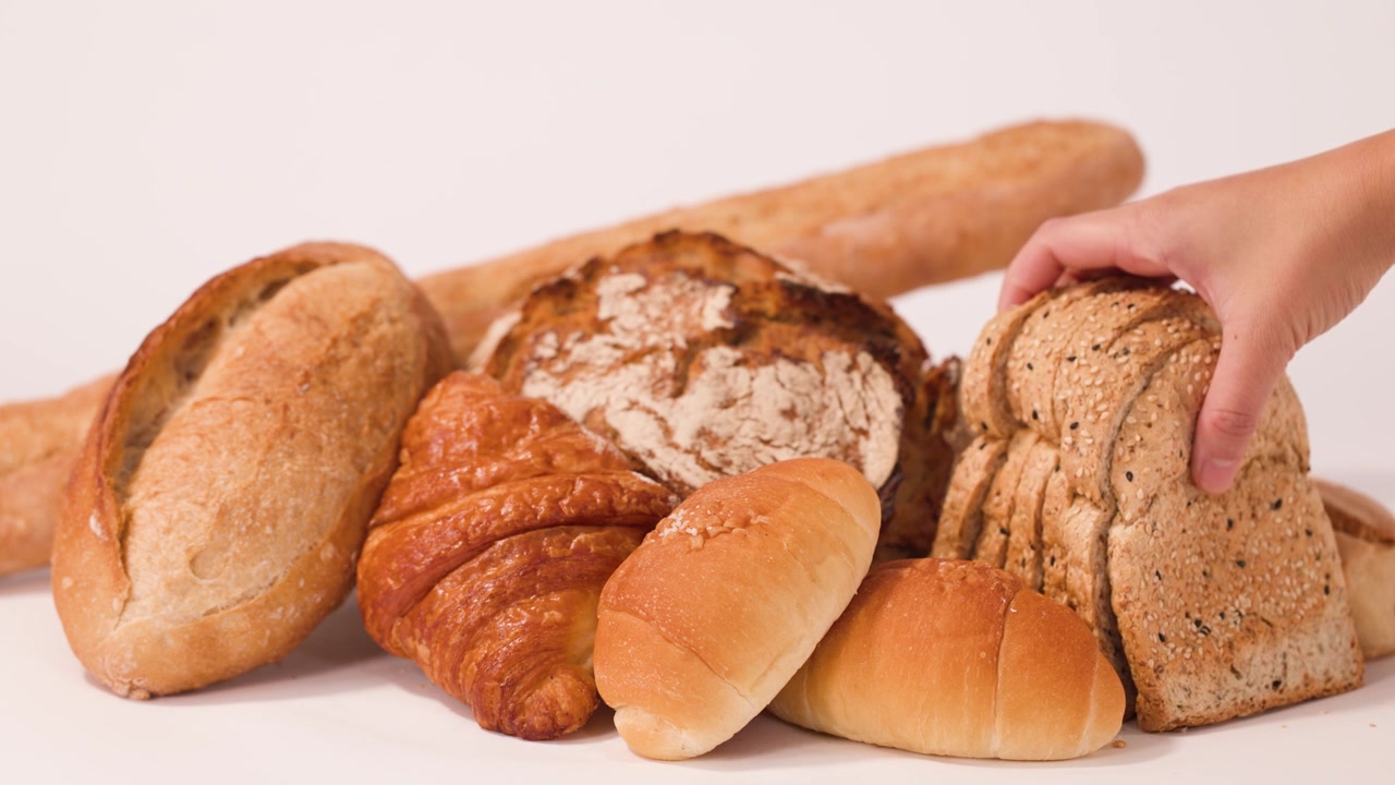 A hand reaches into a variety of fresh breads and selects sliced multigrain loaf.