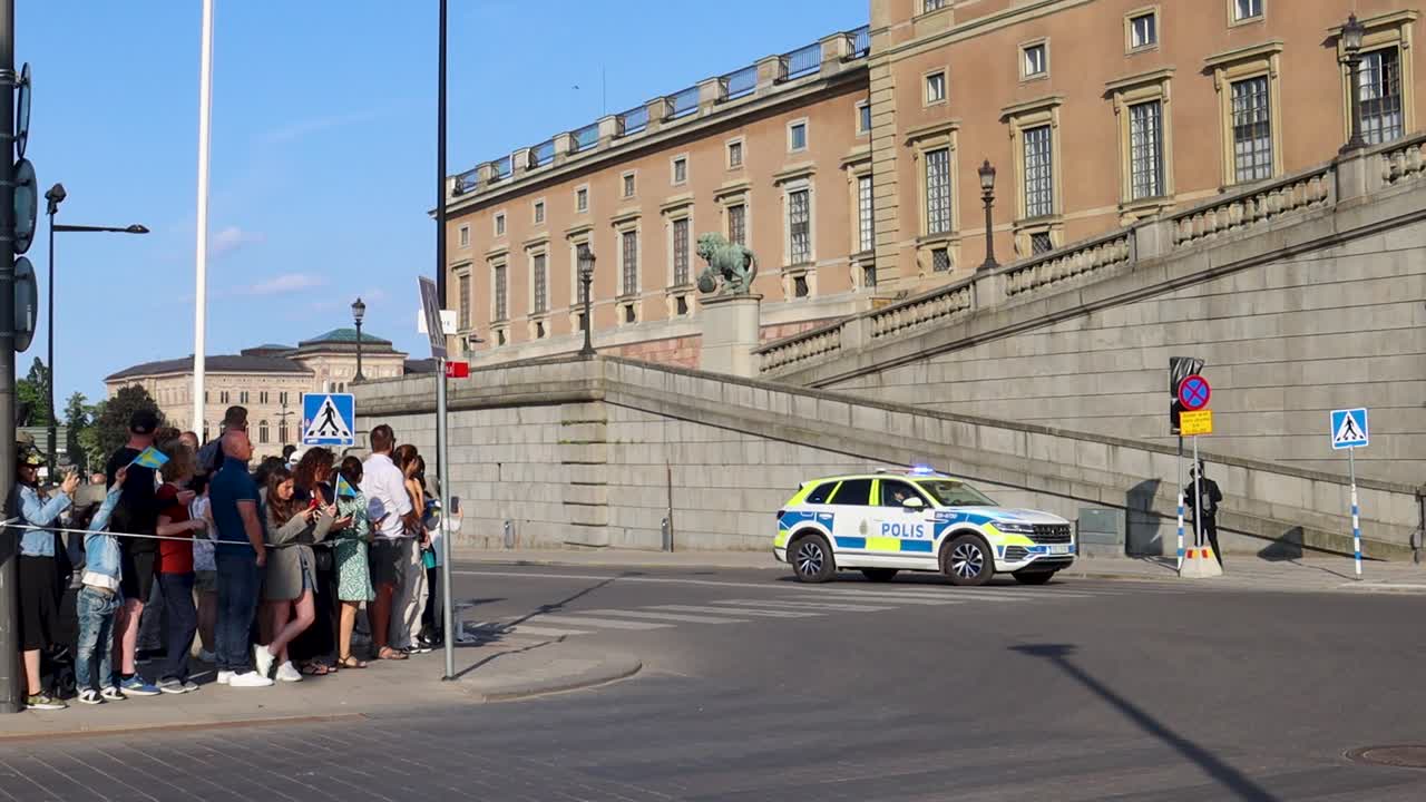 Police car with blinking lights drives by Swedish Royal Palace on National Day