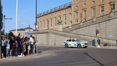 police car with blinking lights drives by swedish royal palace on national day