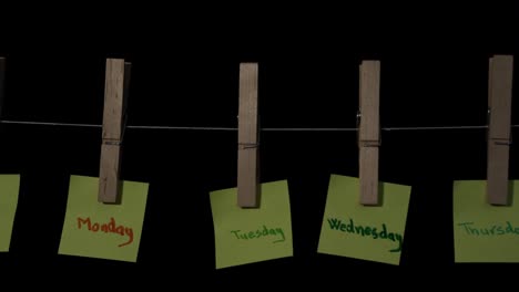 days of the week in yellow sticker labels hanging on wooden sticks with black background