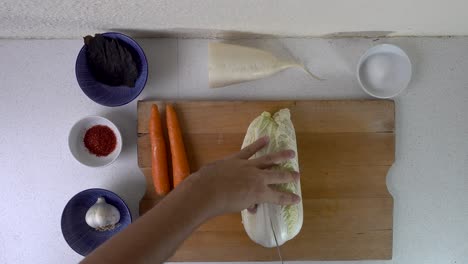 Top-down-look-at-male-hands-cutting-into-and-tearing-apart-whole-cabbage-on-wooden-cutting-board