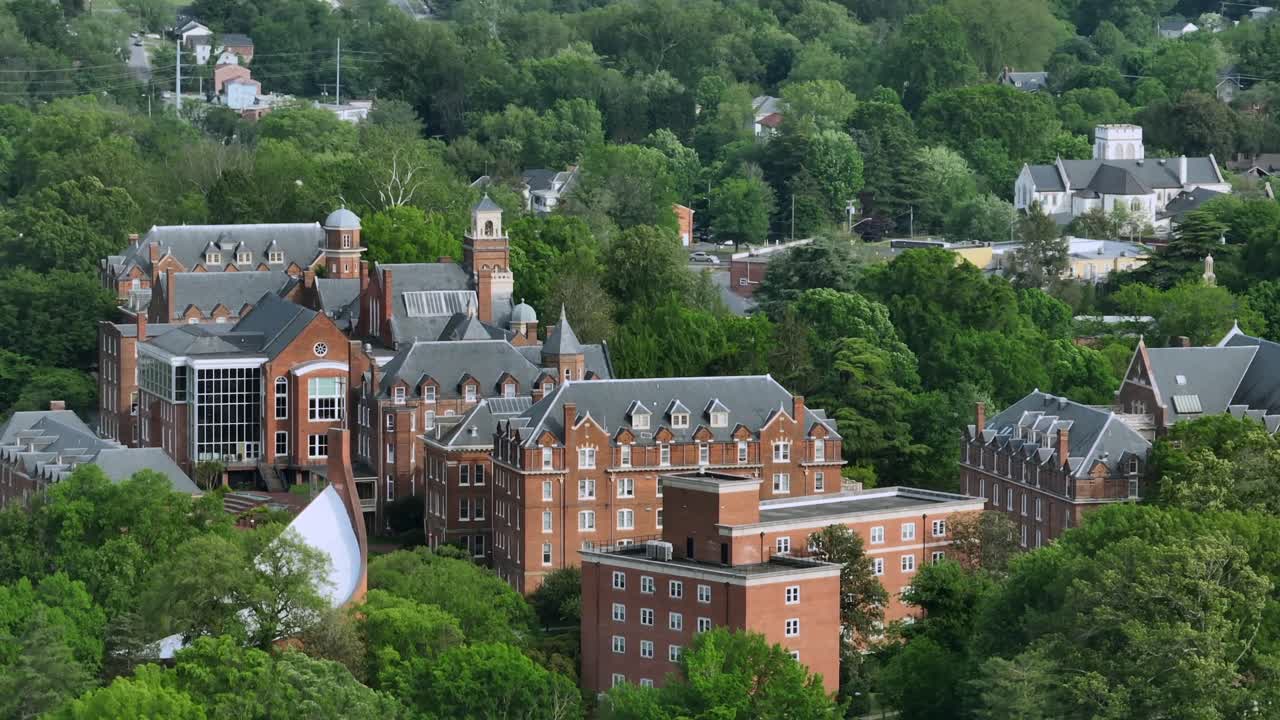 Aerial view of Randolph College in Lynchburg during cloudy day in spring. Wide shot. Green trees in small town. Virginia, USA. Suburb neighborhood with hilly street in distance.