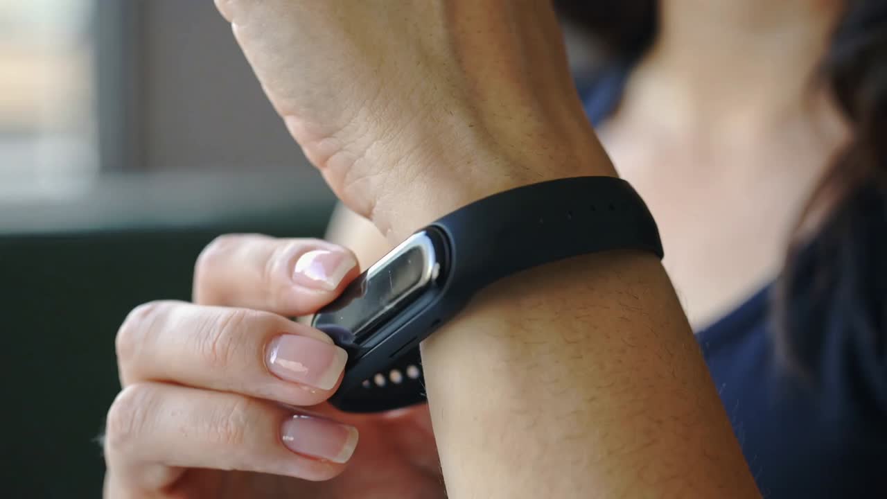 Holding black fitness tracker, woman wearing navy top aligning and securing band onto wrist at home