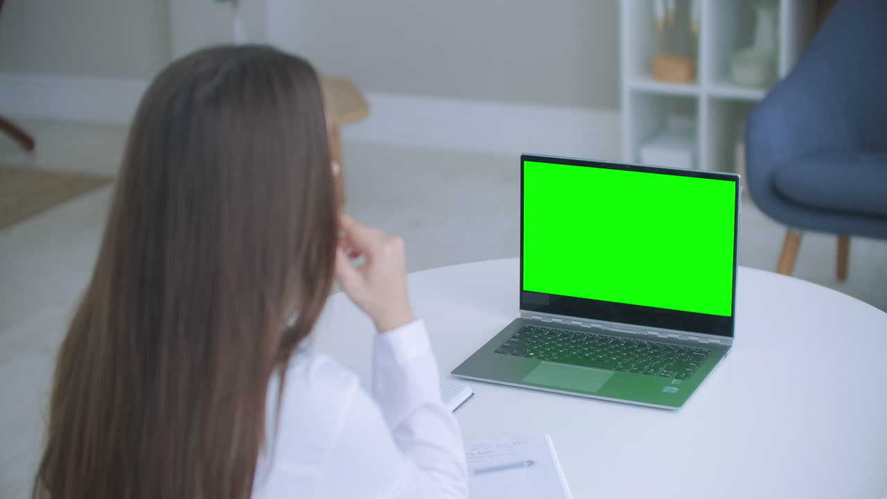 trabajador médico una mujer con una bata blanca utiliza una tableta en la oficina en el escritorio chromakey en la pantalla de la tableta una vista sobre su hombro. médico hablando a la computadora portátil con pantalla verde.