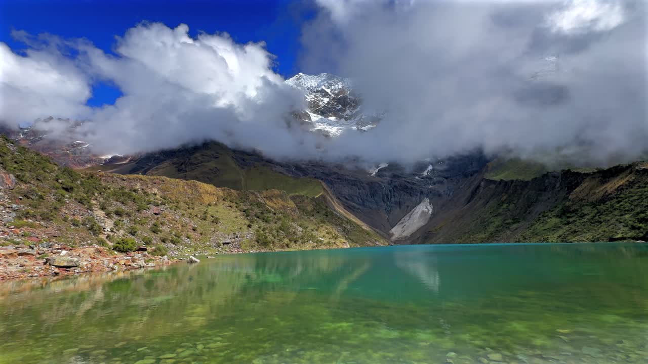 Ande peruviane Monte Humantay Laguna Lago Perù Perú Salkantay alta quota importanti cime montuose innevate con ghiacciaio cielo azzurro mattutino nuvole nebbia provincia di Anta soleggiata stagione secca delle piogge pan left