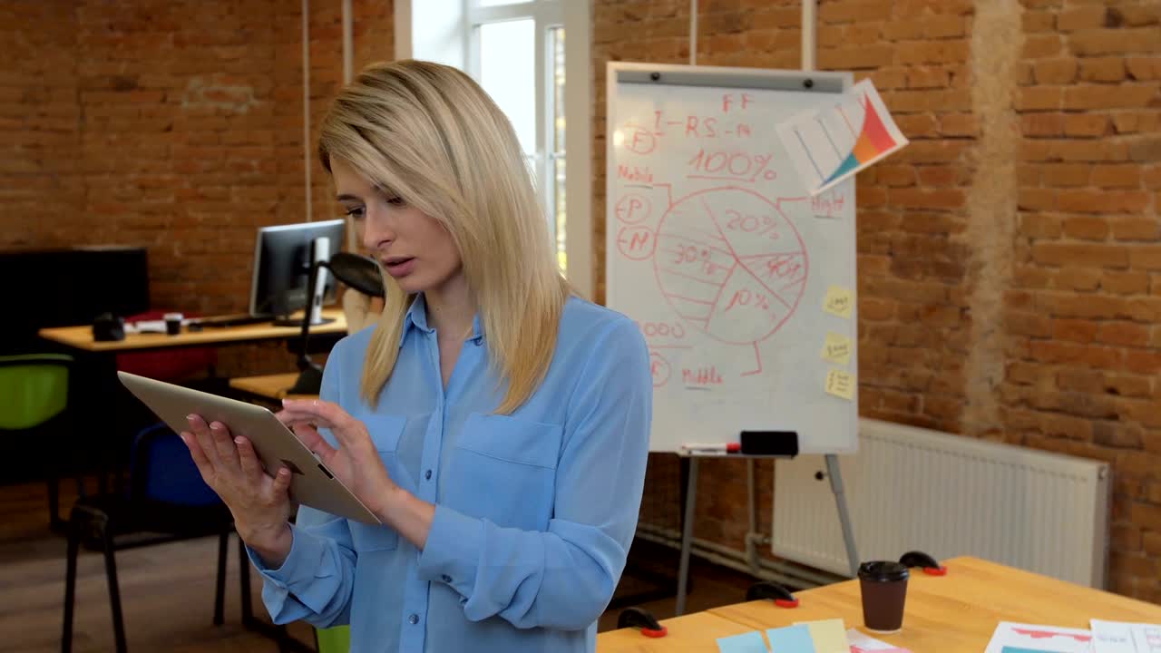 молодая привлекательная женщина использует черный планшет с зеленым экраном в современном офисе.