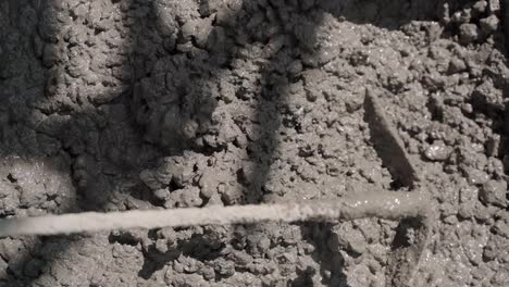 Close-up-slow-motion-shot-of-worker-mixing-cement-on-construction-site-in-sunlight