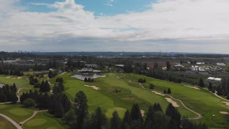 fast approaching wide drone shot of golf course covered in lush green trees grass sand dunes ponds water aerial on sunny cloudy day