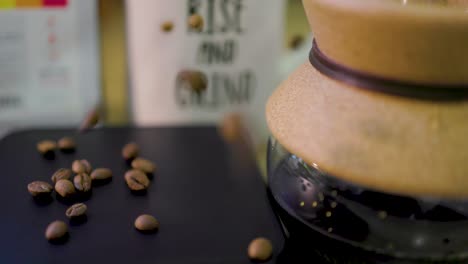 slow-motion-footage-of-coffee-beans-falling-into-the-scene-next-to-a-cup-of-coffee-in-a-beaker-and-coffee-mug