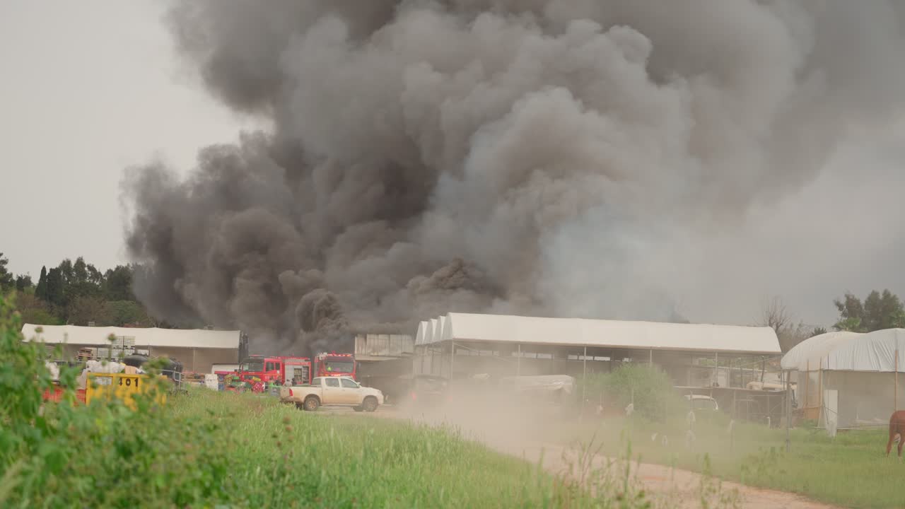 Black smoke clouds and flames rise into the sky from burning warehouses in the village.