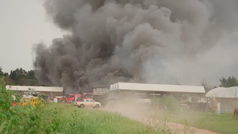 black smoke clouds and flames rise into the sky from burning warehouses in the village.