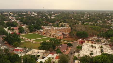 Slide-and-pan-footage-of-medieval-landmark,-old-Convent-of-San-Bernardino-de-Siena.-Trees-and-buildings-in-town-around.-Valladolid,-Mexico