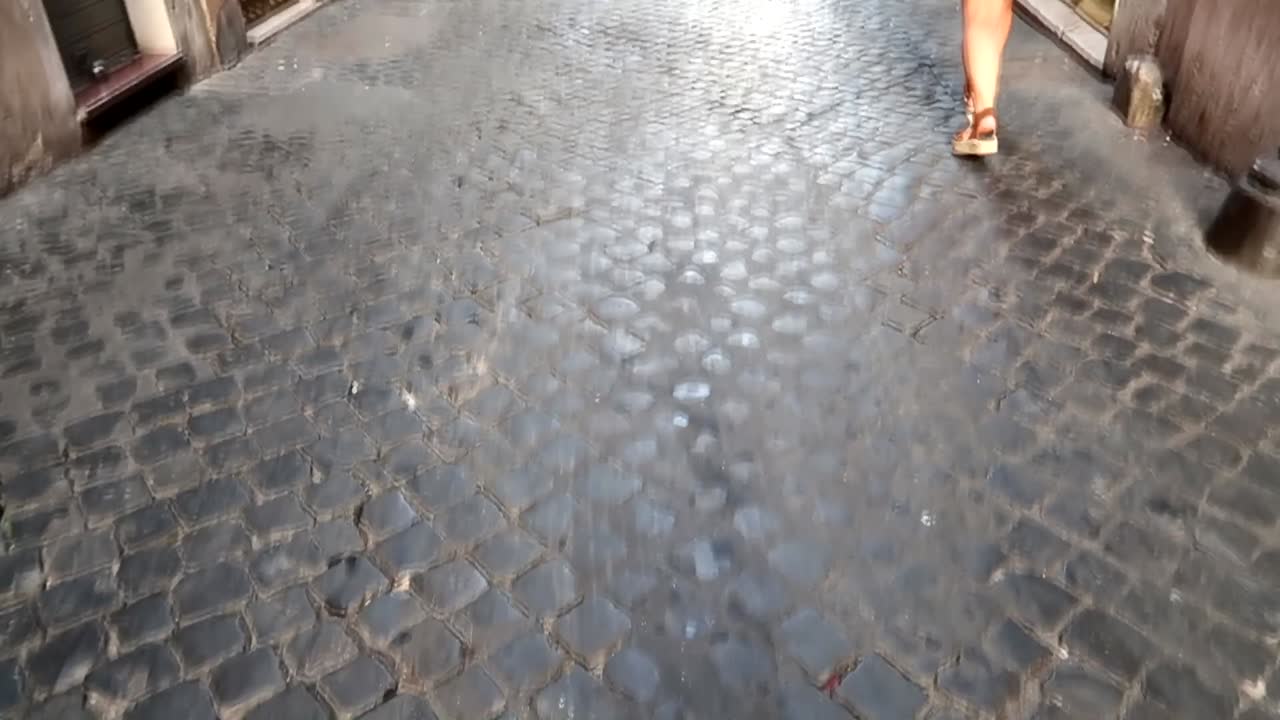 손에 모자를 들고 오렌지색 옷을 입은 여자가 이탈리아 로마의 작은 돌길을  ⁇ 고 있습니다.