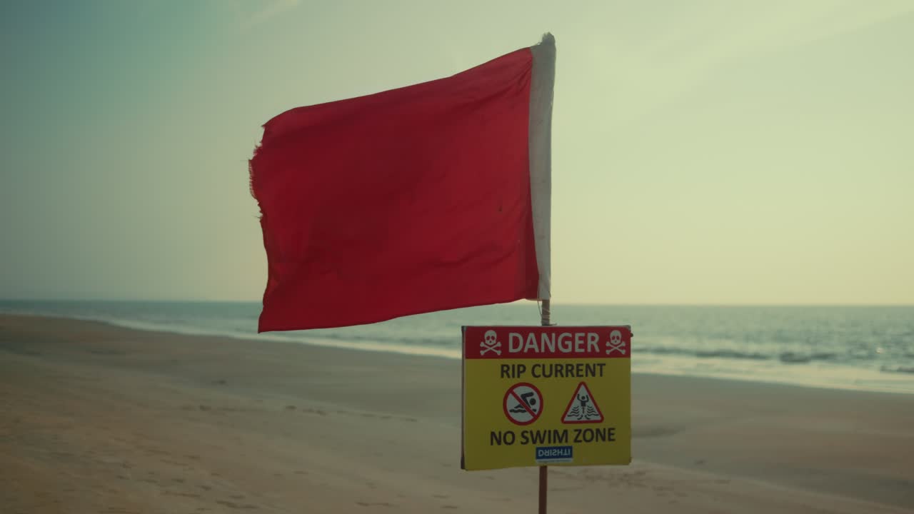 Red flag on beach warning of rip currents, creating a tense atmosphere