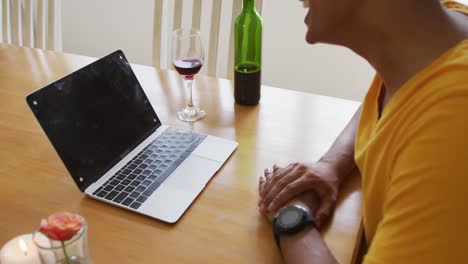 Midsection-of-mixed-race-man-sitting-at-table-making-video-call-with-laptop