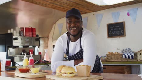 portrait of african american man wearing apron smiling while standing in the food truck